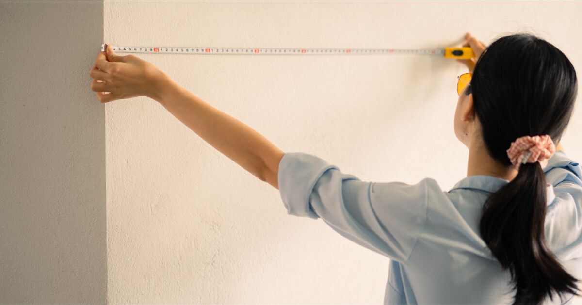 A female measuring the wall with measuring tape