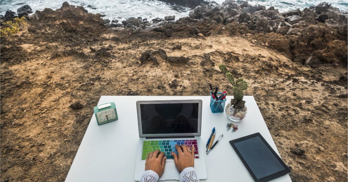 Person using a laptop on a work desk that's on a seashore