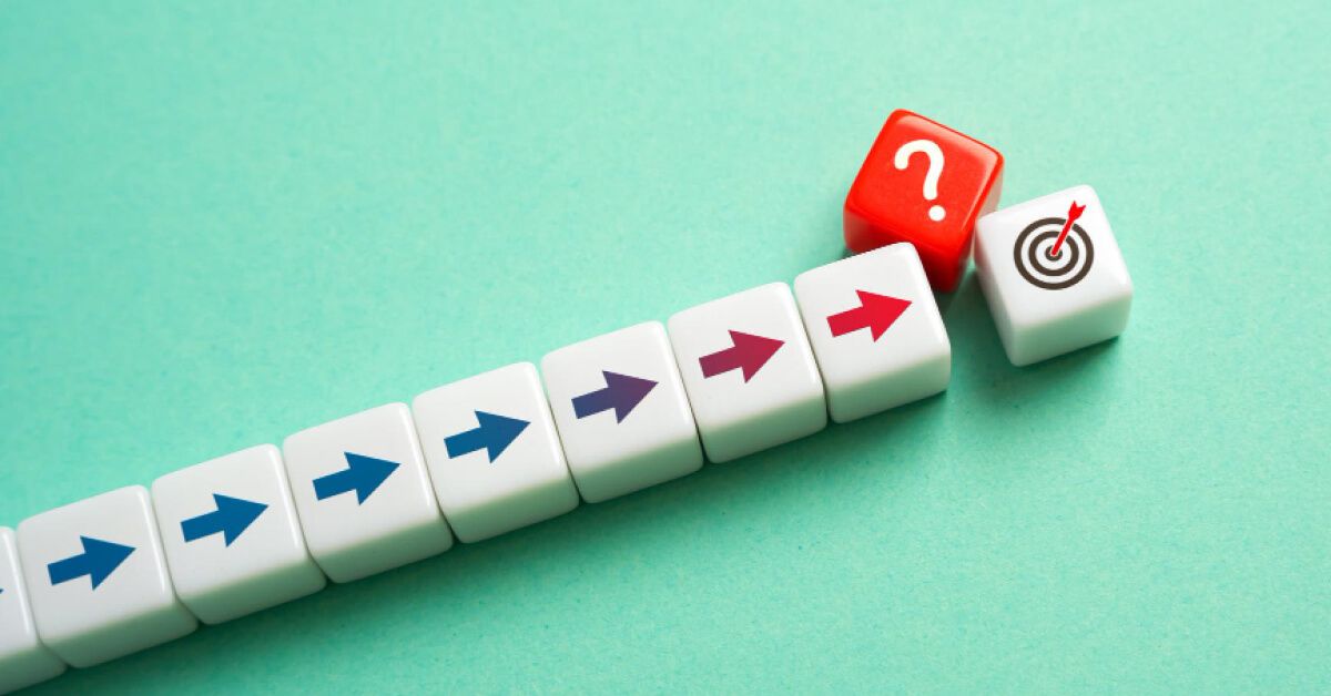 A red block with question mark blocking a series of white blocks with arrows that are moving towards a block with a target board graphic