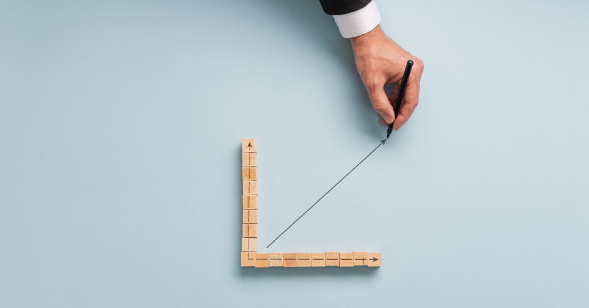 Person drawing an upward moving graph line within a wooden block graph