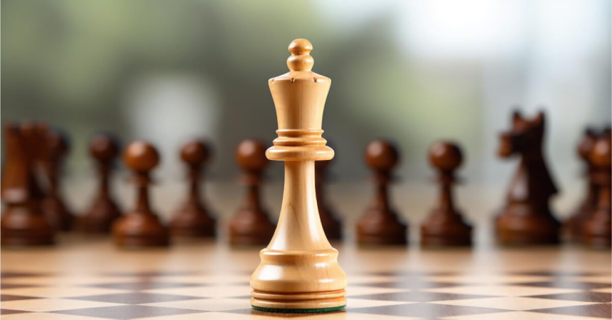 Focused shot of a white king chess piece with black chess pieces lined up behind it