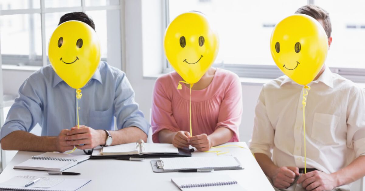 Employees holding yellow balloons with smiley faces in front of their faces