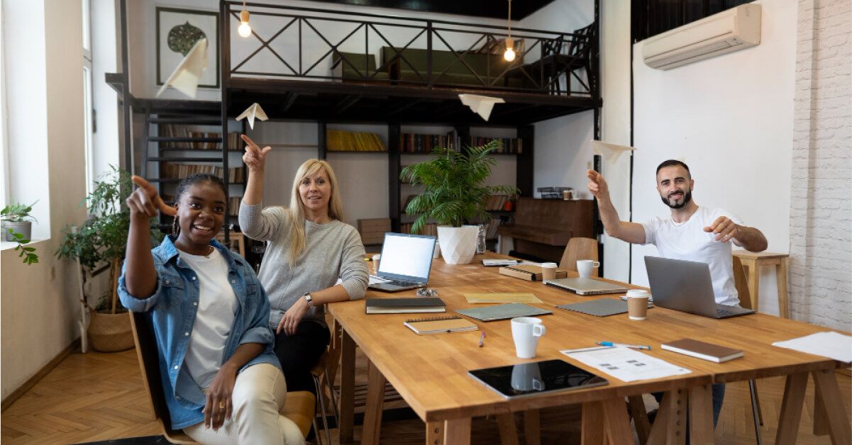 Diverse group of employees launching paper planes around a table