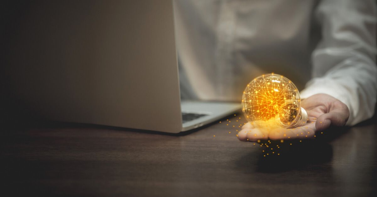 Person holding a holographic lightbulb while using a laptop