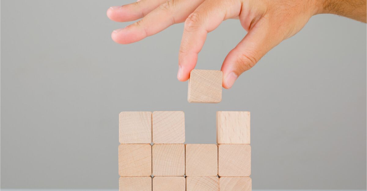 Hand placing cube wooden blocks on top of each other
