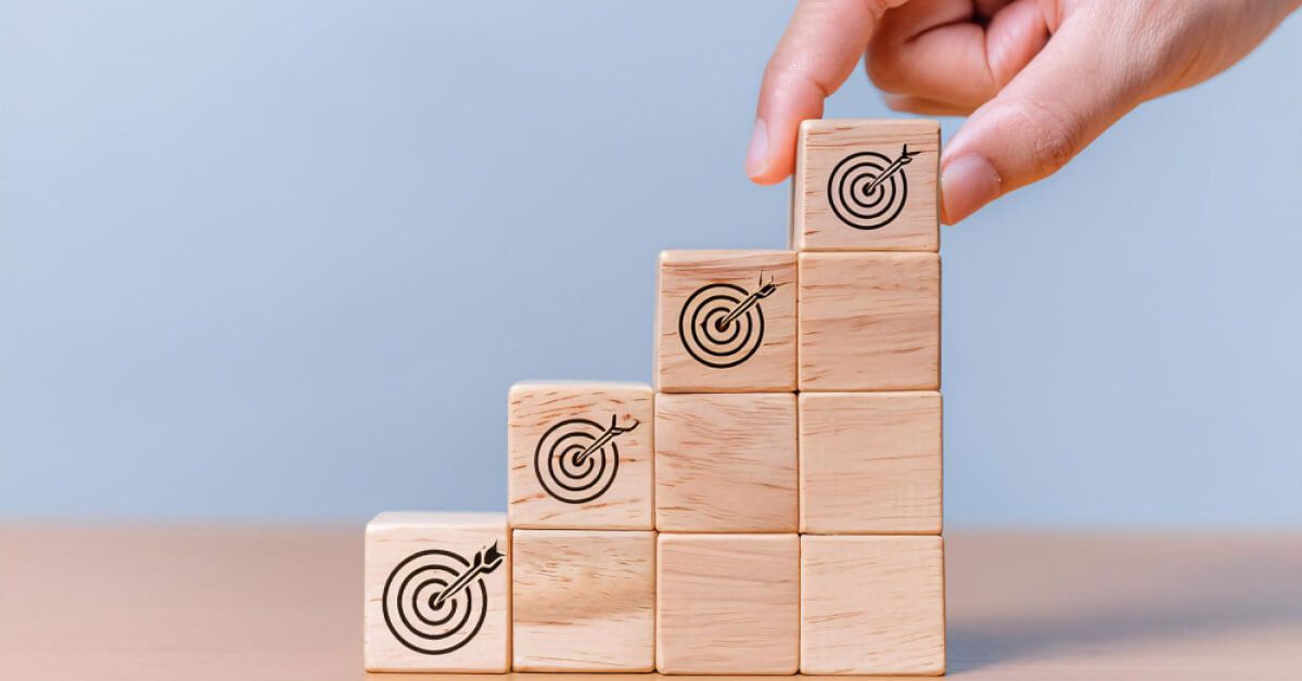 Person placing a wooden block with a target board graphic on top of a set of wooden blocks
