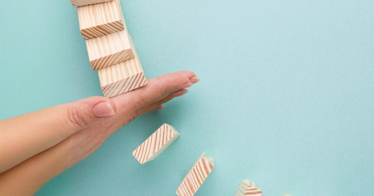 Person blocking a series of wooden blocks from falling over