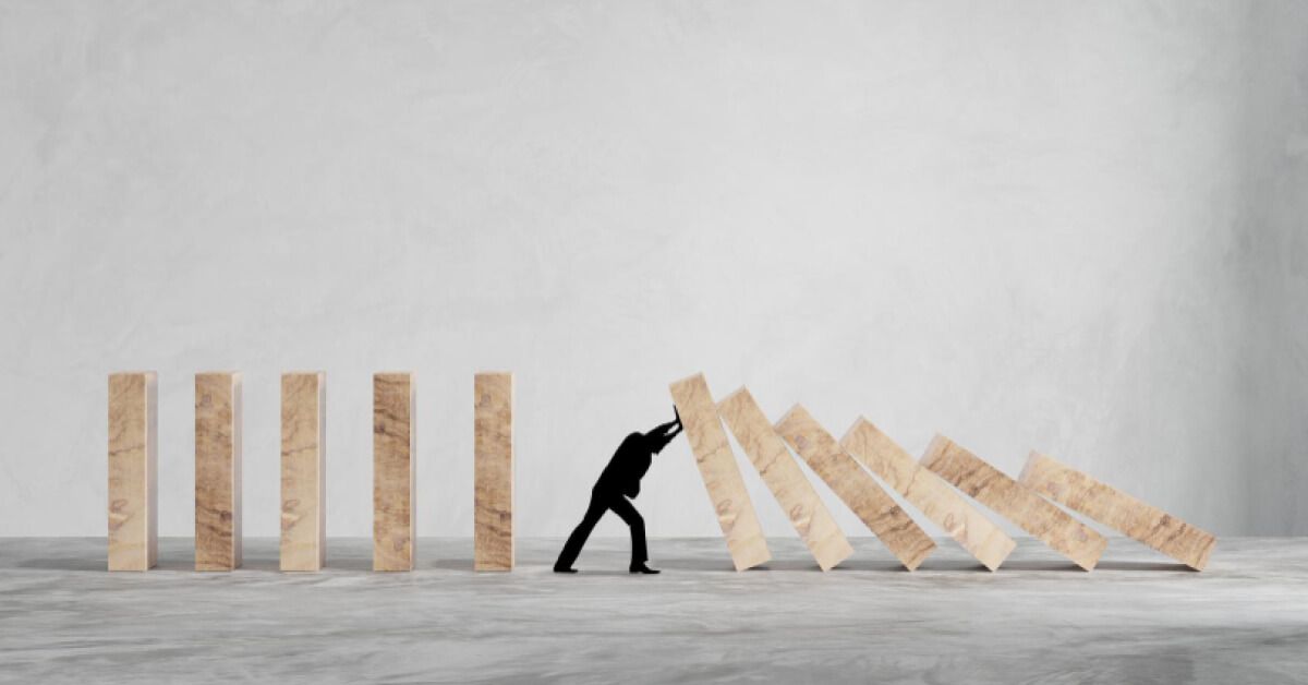 Silhouette of a person stopping a series of wooden blocks from falling over