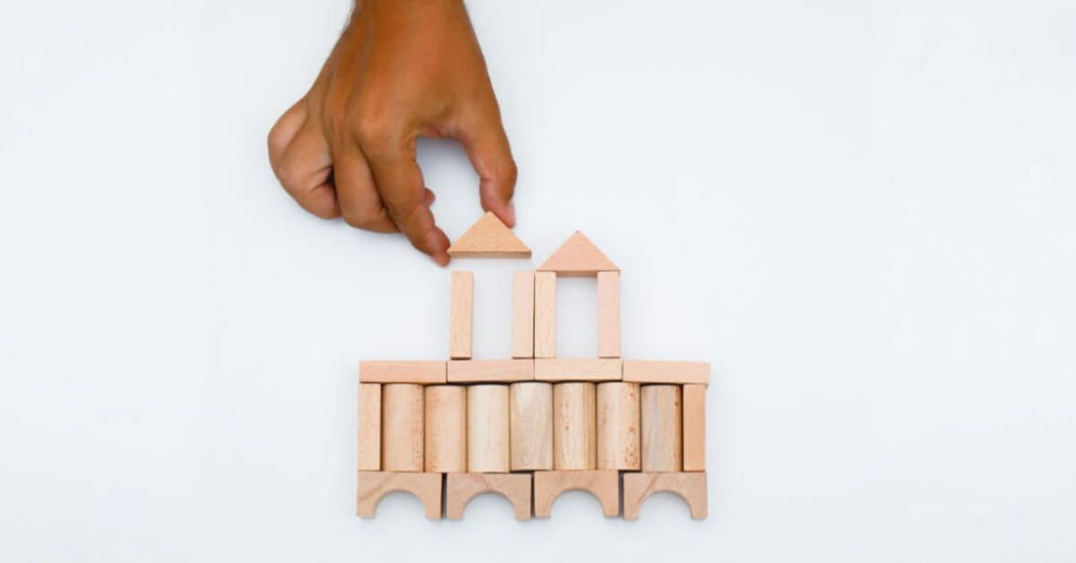 Person placing a triangular wooden piece on top of a structure of wooden blocks