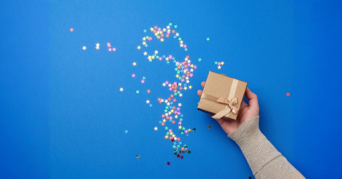 Person holding a gift box with sparkly stars around it