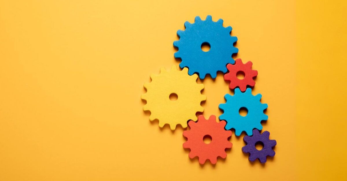 Multicoloured interlocked gears over a yellow backdrop