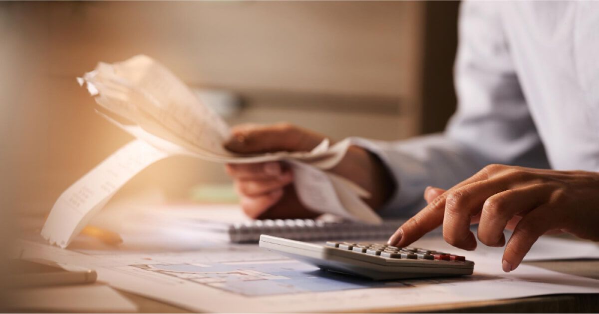 Person using a calculator with a set of bills on the other hand