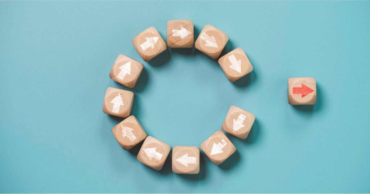 Wooden block with red arrow moving away from a circle of wooden blocks with white arrows