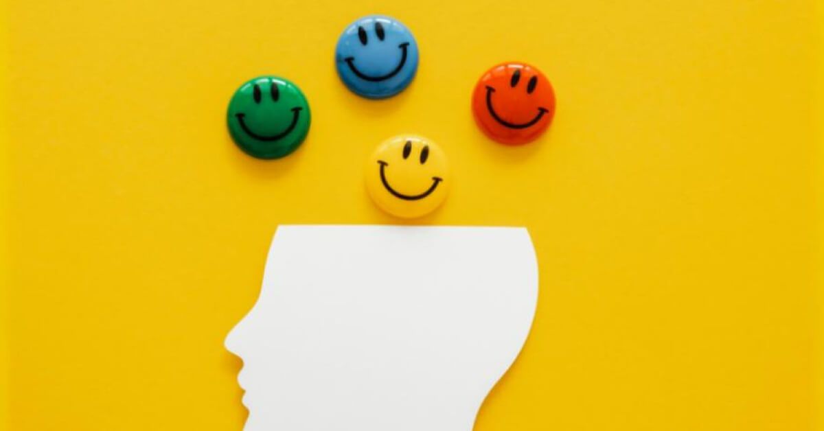 Multicoloured emoticon pins over a paper cutout of a head