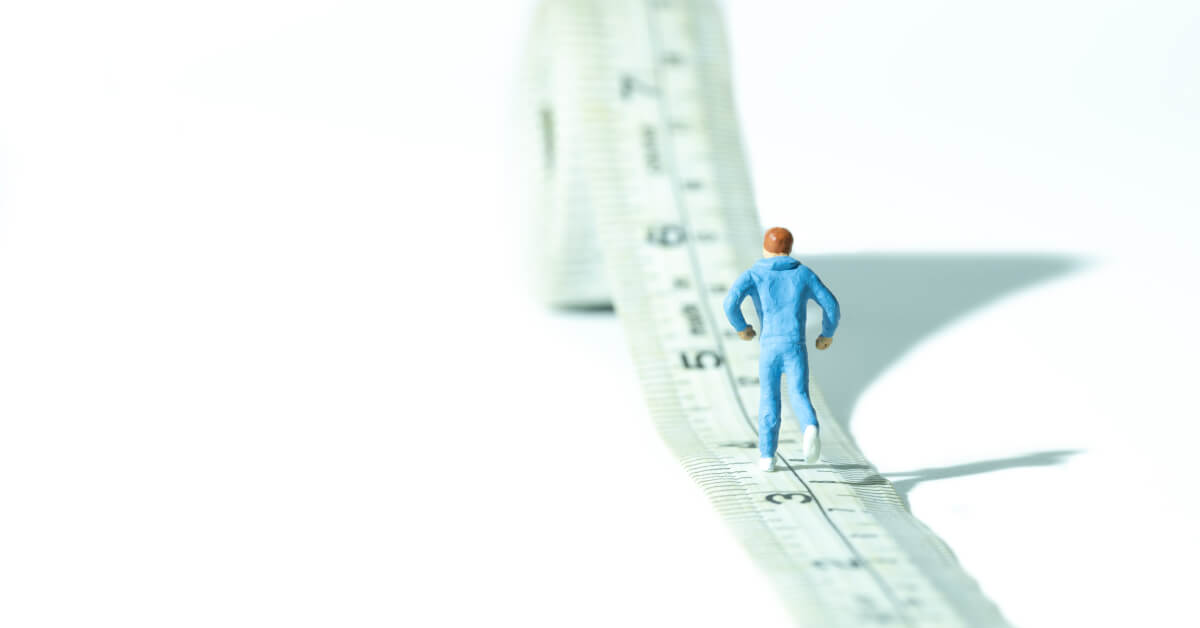 Miniature figurine walking over a white measuring tape
