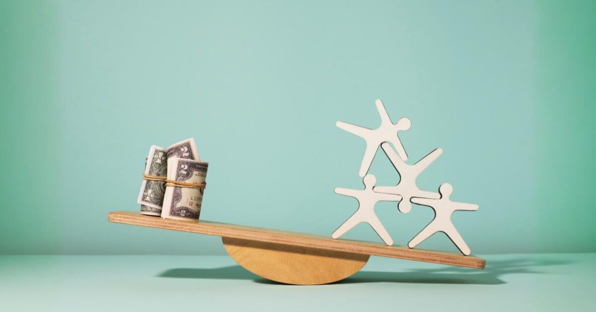 A set of wooden figurines and money at opposite ends of a wooden balancing scale