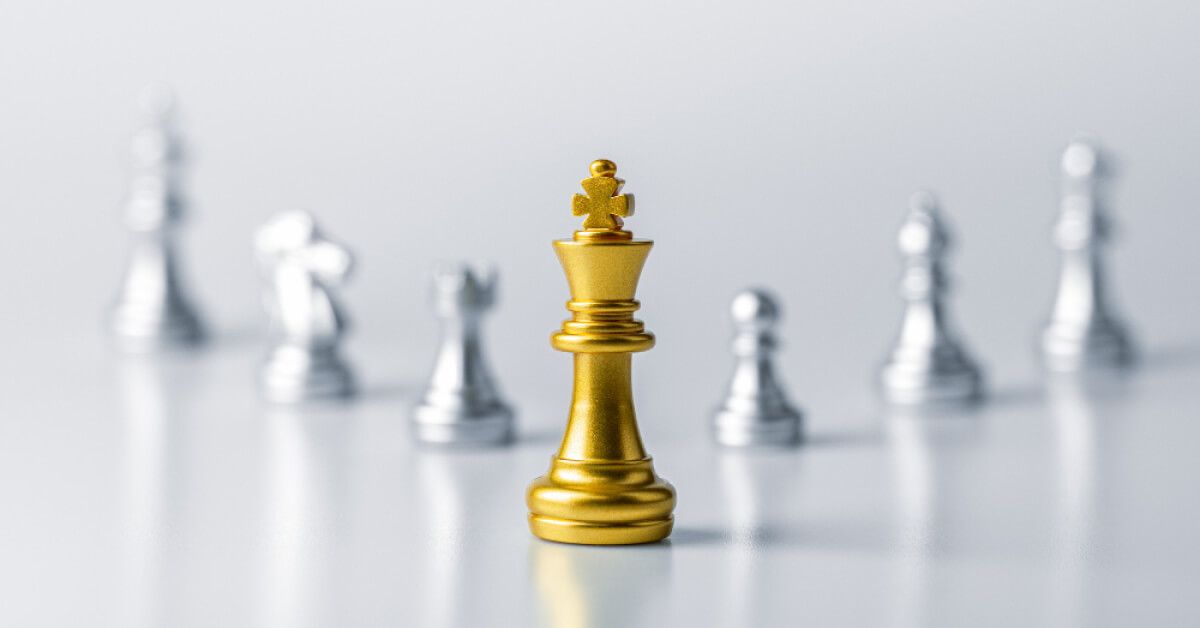 Golden chess king piece in front of other silver pieces