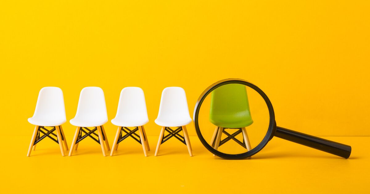 Magnifier glass over a green chair in a lineup of white chairs