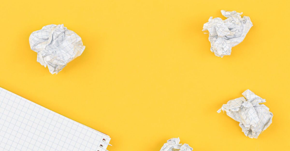 Crushed up paper balls around a notebook against a yellow backdrop
