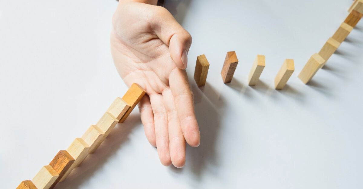 Person stopping a series of wooden blocks from falling over