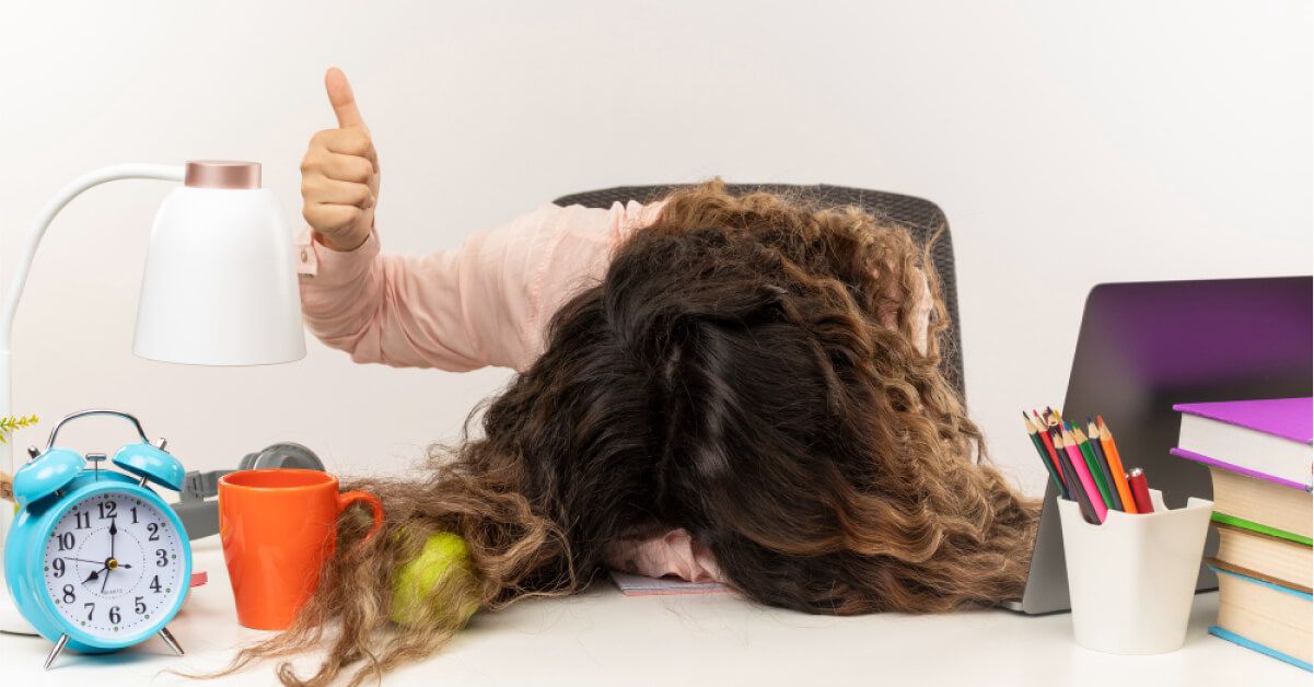 An employee banging her head against her table desk, who's signaling okay but doesn't actually look ok