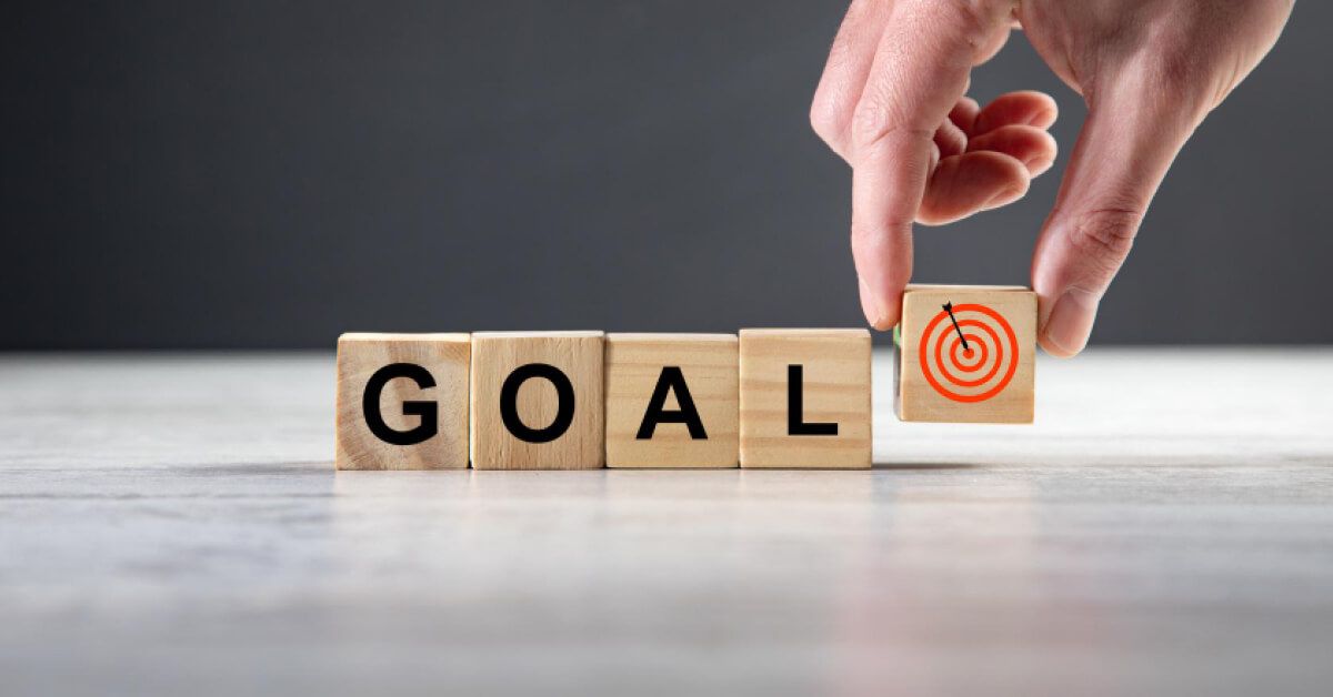 Person placing a wooden block with a target graphic next to a series of wooden blocks spelling "GOAL"