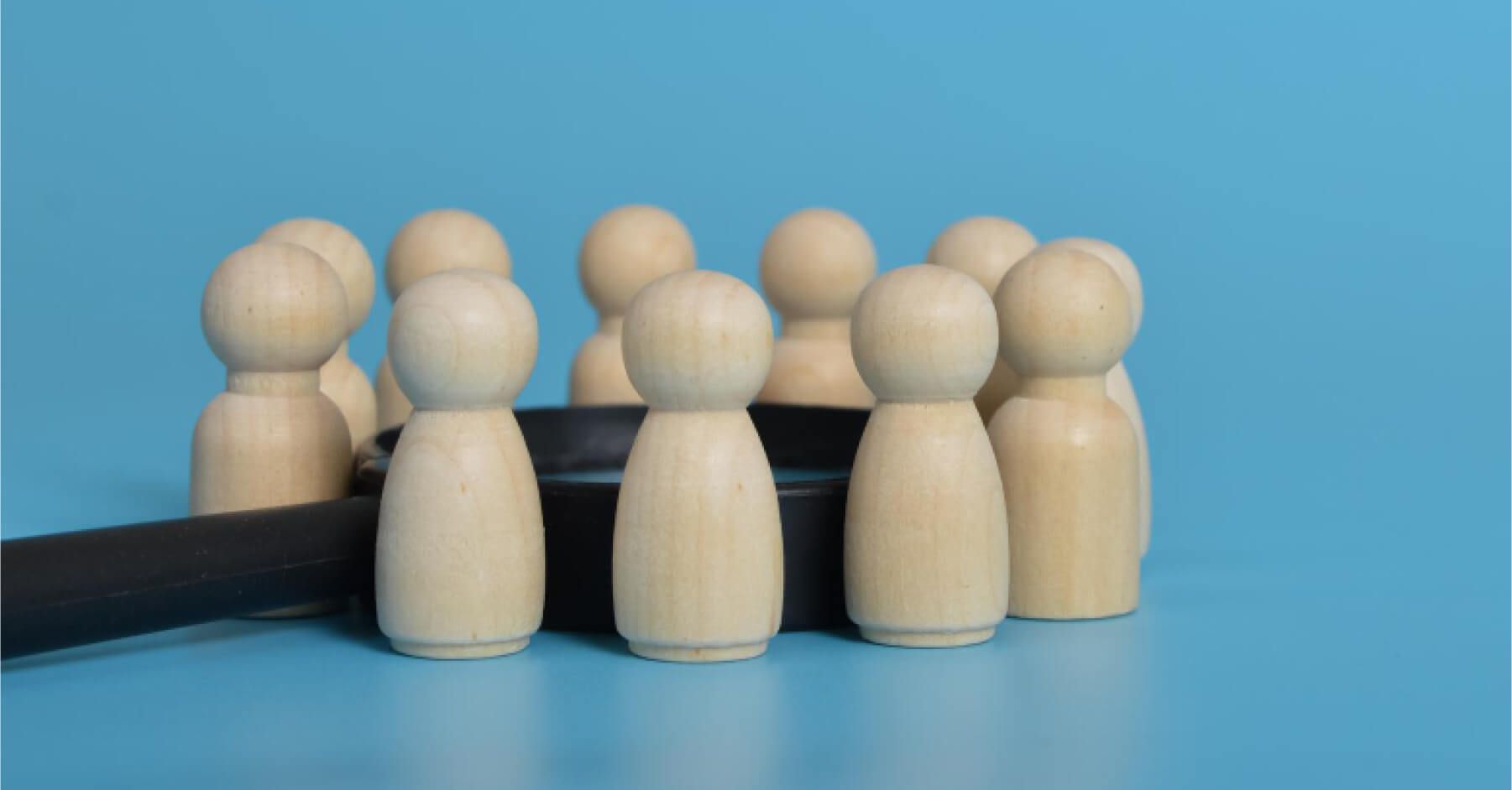 Wooden pawns of humans surrounding a magnifying glass