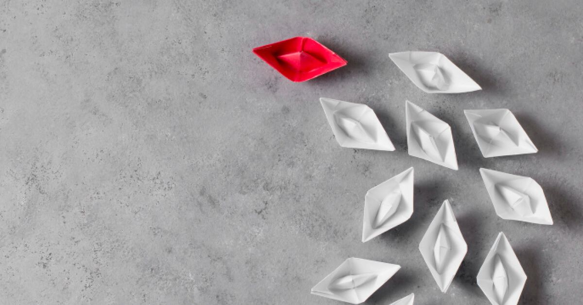 Red paper boat alongside a group of white paper boats