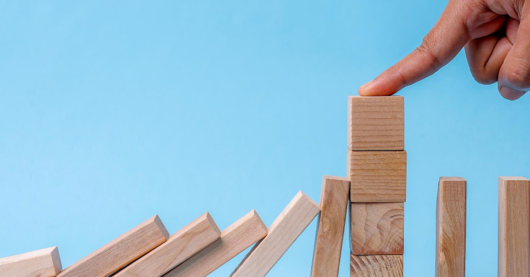 Person stopping a series of wooden blocks from falling over