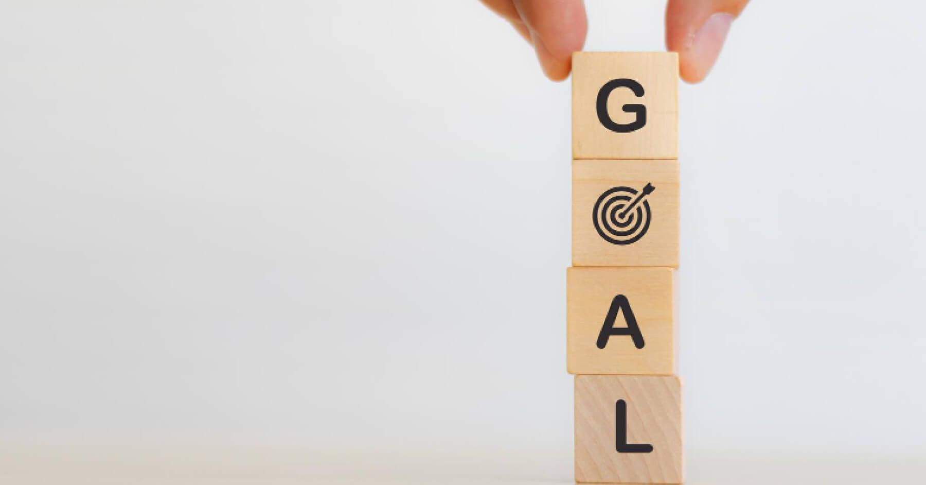 Person stacking wooden blocks to spell the word 'GOAL'