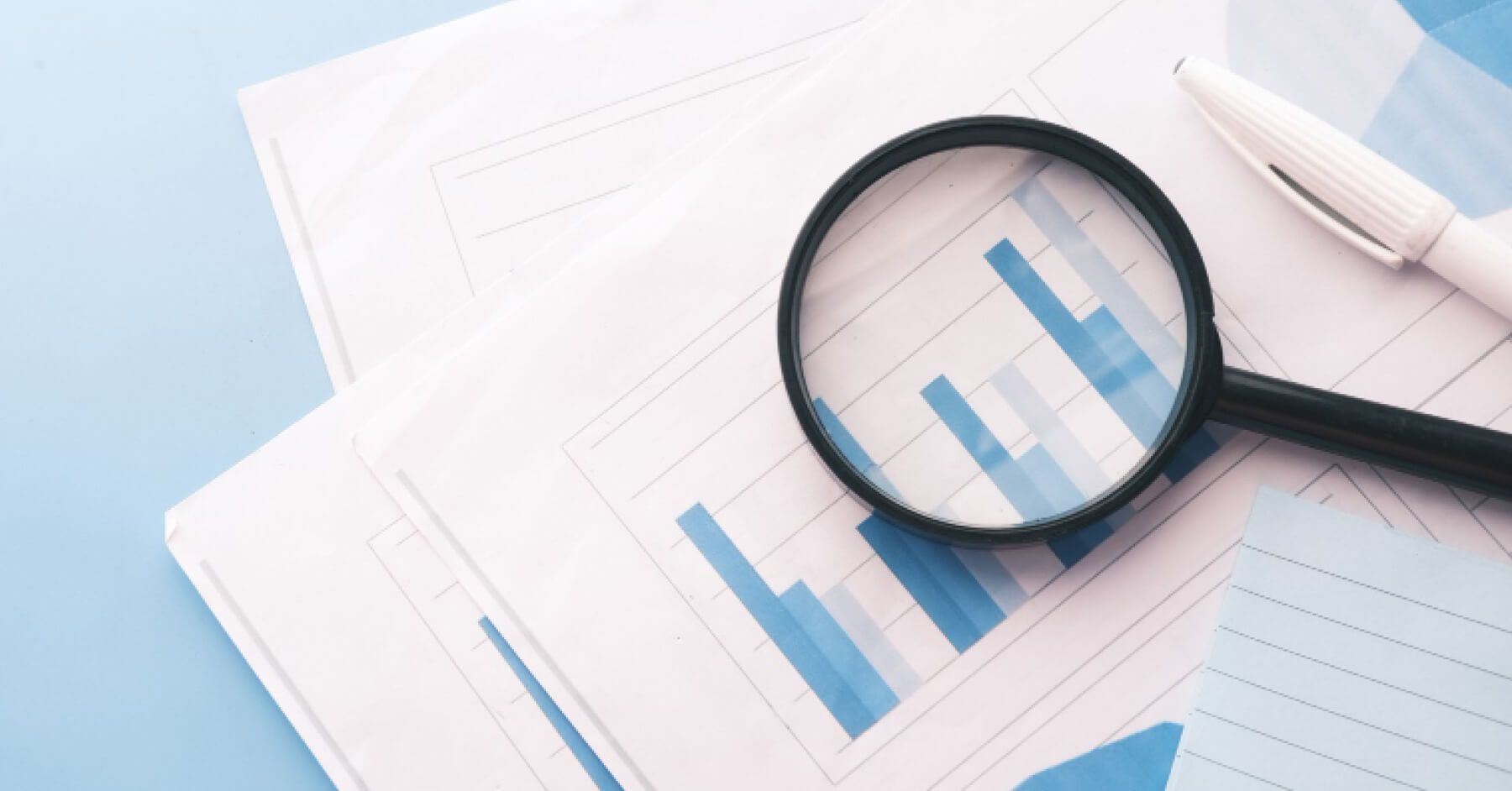 Magnifier glass and pen on top of reports and graphs