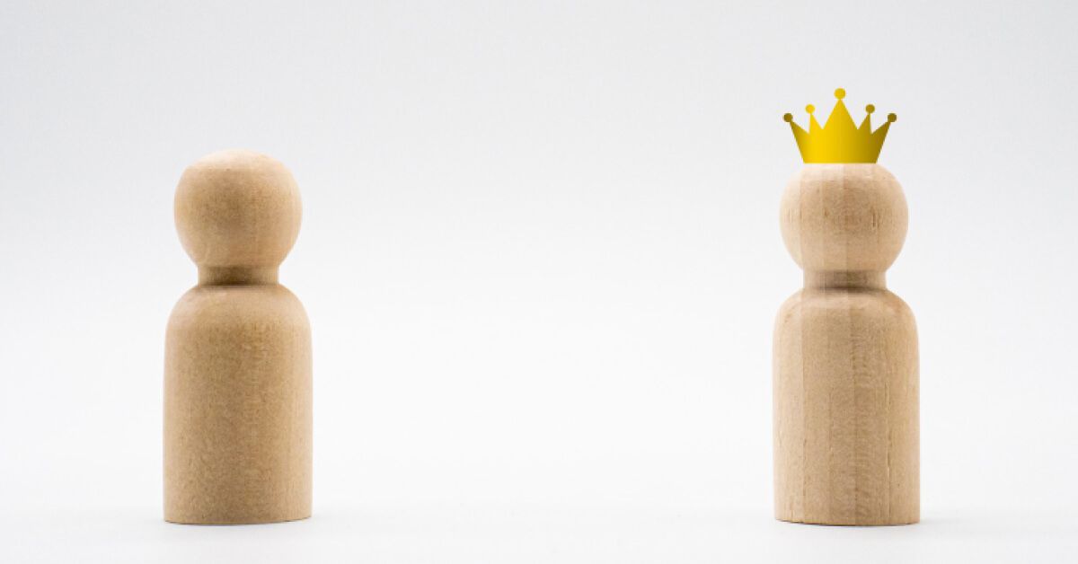 Two wooden pawns of one being plain and the other with a crown
