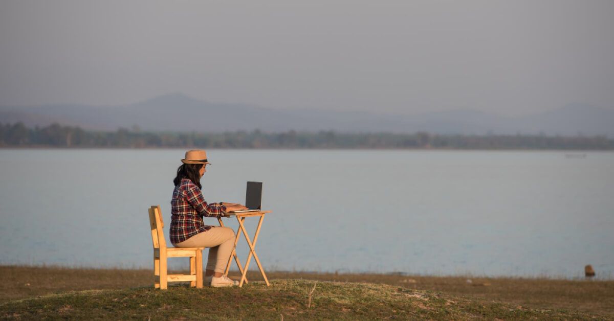 Remote working woman sitting and working near a river