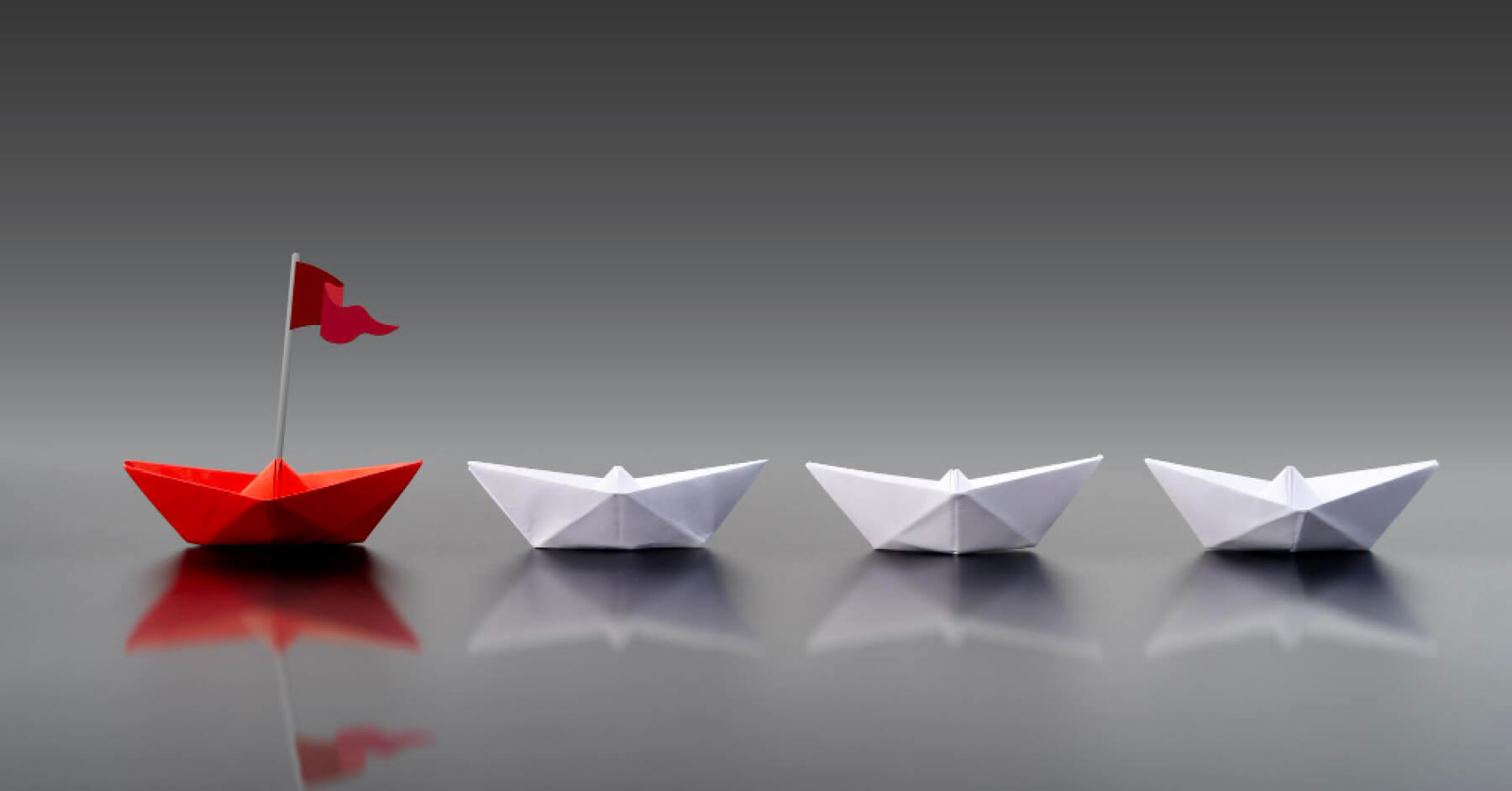 Three white paper boats and one red paper boat with a red flag