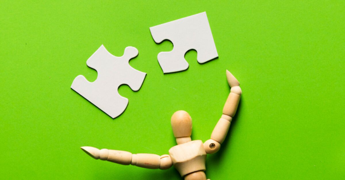 Wooden toy near 2 white puzzle pieces against a green background