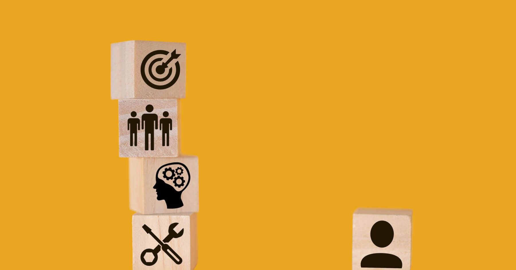 Stacked wooden blocks of target, people, ideas and tools next to a wooden block of an employee against a yellow background