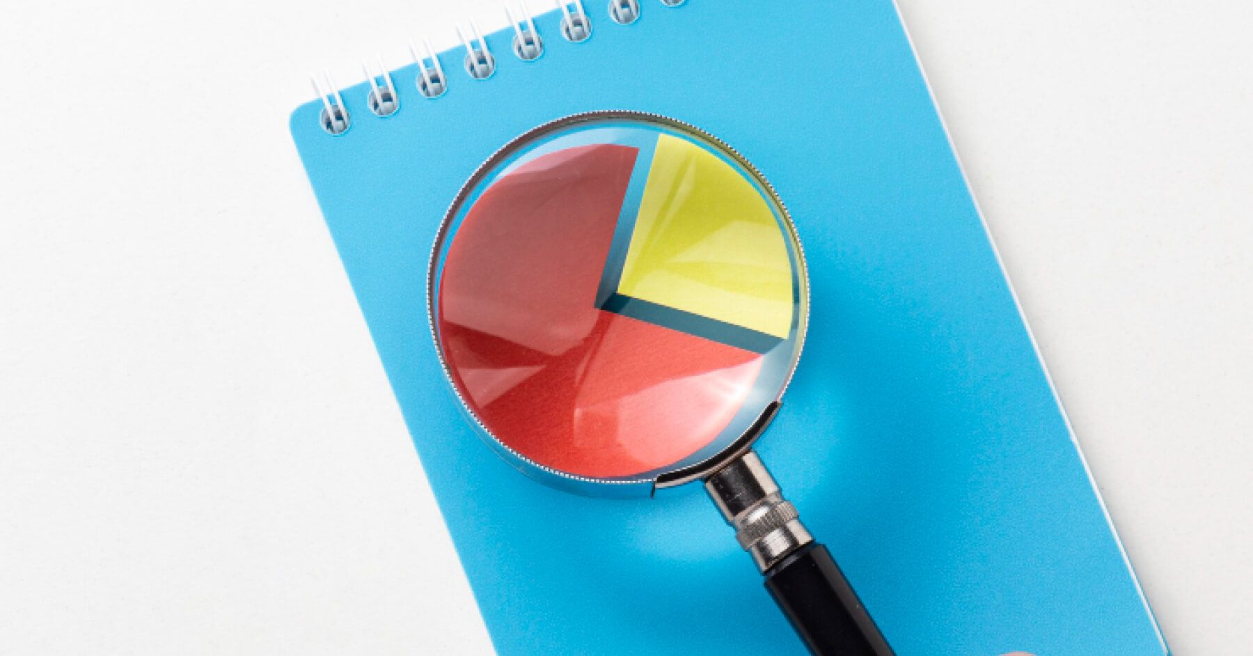 A magnifying glass zooming on a pie chart in a blue notebook