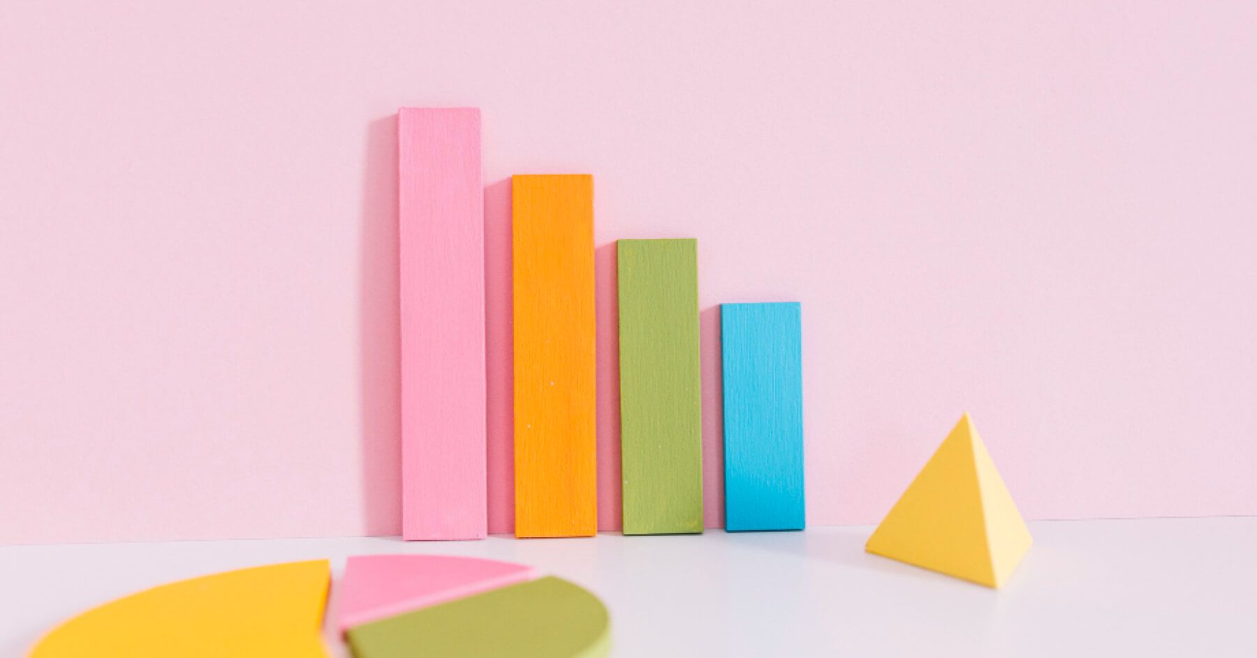 Pie chart, triangle and statistics bars 3d wooden objects placed against a pink background
