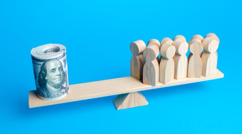 Money and wooden blocks of employees balanced against each other