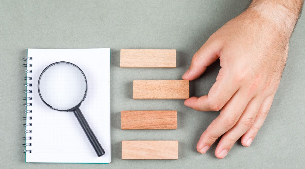 Hand holding wooden block next to a magnifying glass on a notebook