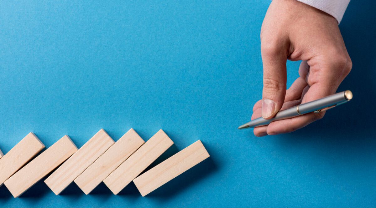Man holding a pen next to domino wooden blocks 