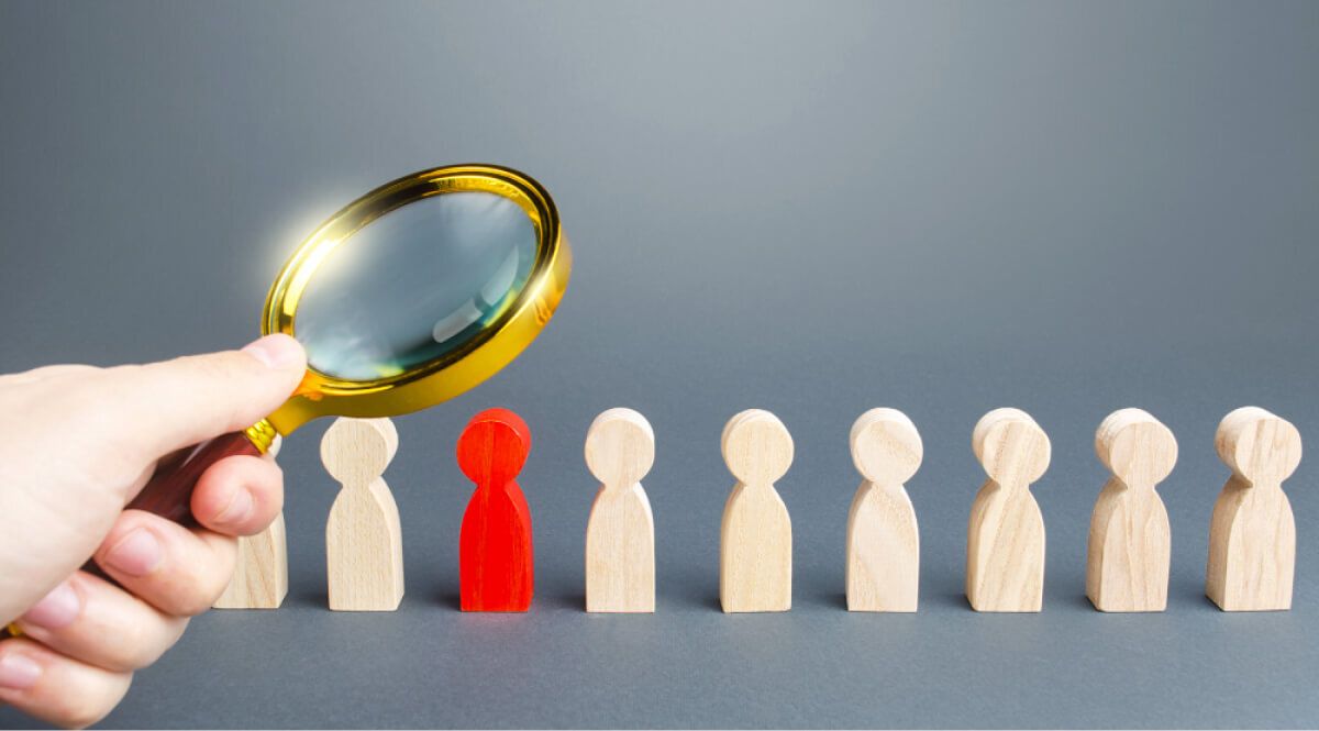 Man looking at wooden blocks shaped as people through a golden magnifying glass