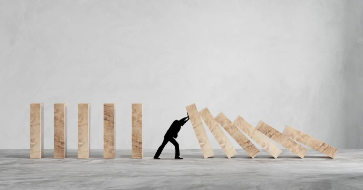Silhouette of a person stopping a series of wooden blocks from falling over